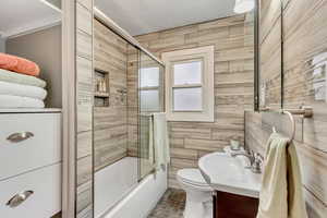 Full bathroom with toilet, shower / bath combination with glass door, tile walls, and vanity