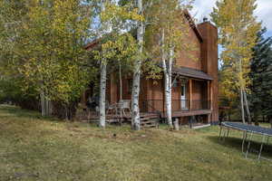 View of side of home with a wooden deck, a yard, and a trampoline