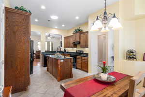 Kitchen with light tile patterned flooring, kitchen peninsula, ceiling fan with notable chandelier, dark stone counters, and black appliances