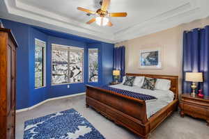 Carpeted bedroom with a raised ceiling and ceiling fan