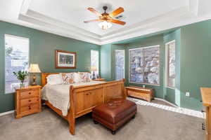 Bedroom featuring ceiling fan, light colored carpet, and a tray ceiling