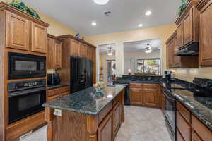 Kitchen with sink, a center island, black appliances, and dark stone counters