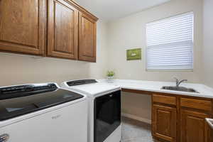 Clothes washing area featuring sink, cabinets, washing machine and clothes dryer, and light tile patterned floors