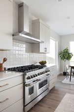 Kitchen featuring white cabinets, decorative backsplash, range with two ovens, wall chimney range hood, and dark wood-type flooring