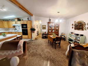 Dining area with light colored carpet, a notable chandelier, and lofted ceiling with beams