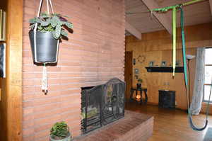 Living room featuring a brick fireplace, beam ceiling, wooden walls, and wood-type flooring