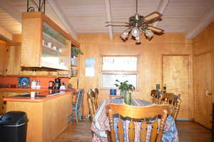 Dining space featuring wood walls, ceiling fan, beamed ceiling, and hardwood / wood-style floors