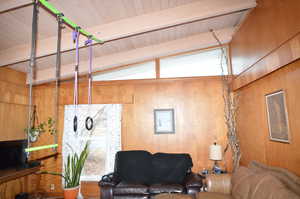 Living room featuring wooden ceiling, wooden walls, and vaulted ceiling with beams