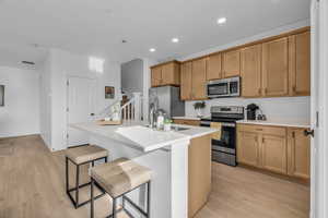 Kitchen with light hardwood / wood-style flooring, a center island with sink, appliances with stainless steel finishes, a kitchen breakfast bar, and sink