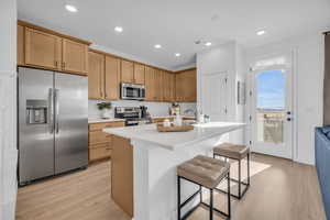 Kitchen featuring stainless steel appliances, a breakfast bar area, light hardwood / wood-style floors, and an island with sink