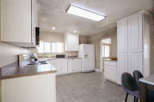 Kitchen featuring sink, white cabinets, a textured ceiling, white appliances, and light tile patterned floors