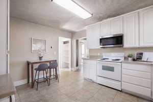 Kitchen with white cabinetry, white electric range, a kitchen bar, and light tile patterned floors