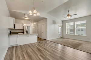 Kitchen featuring white cabinetry, vaulted ceiling, ceiling fan with notable chandelier, hanging light fixtures, and stainless steel fridge