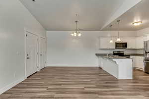 Kitchen featuring white cabinets, appliances with stainless steel finishes, a kitchen breakfast bar, and hanging light fixtures