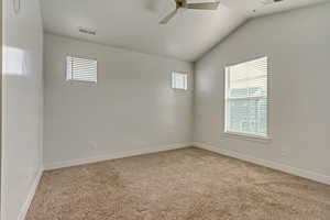 Empty room featuring ceiling fan, light colored carpet, vaulted ceiling, and a wealth of natural light