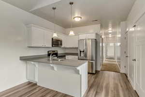 Kitchen featuring white cabinets, pendant lighting, kitchen peninsula, and appliances with stainless steel finishes