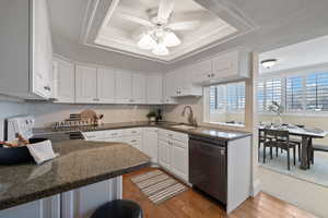 Kitchen with a tray ceiling, white cabinetry, dishwasher, and sink