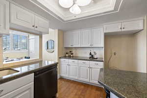 Kitchen with hardwood / wood-style floors, backsplash, white cabinets, a raised ceiling, and black dishwasher