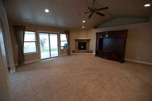 Unfurnished living room with ceiling fan, vaulted ceiling, and light carpet