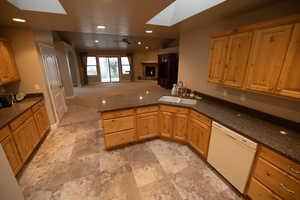 Kitchen featuring sink, a tile fireplace, ceiling fan, dark stone countertops, and white dishwasher