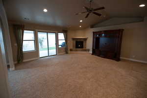 Unfurnished living room featuring a tiled fireplace, ceiling fan, vaulted ceiling, and light colored carpet