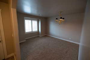 Carpeted spare room featuring a notable chandelier