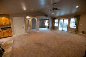 Unfurnished living room with light carpet, ceiling fan, and vaulted ceiling