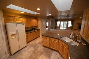 Kitchen with white refrigerator with ice dispenser, ceiling fan, dark stone countertops, and sink