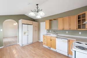 Kitchen with sink, vaulted ceiling, white appliances, light hardwood / wood-style floors, and hanging light fixtures