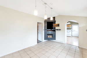 Kitchen with a tile fireplace, lofted ceiling, light tile patterned flooring, white electric range oven, and hanging light fixtures