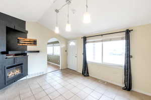 Unfurnished living room with a tiled fireplace, vaulted ceiling, and light tile patterned floors