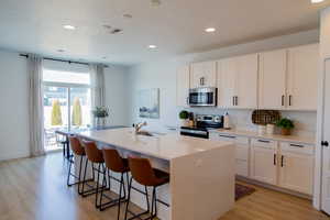 Beautiful Kitchen with stainless steel appliances, sink, white cabinets, light laminate floors, and oversized island waterfall white quartz island