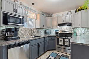 Kitchen featuring range hood, pendant lighting, light tile patterned floors, appliances with stainless steel finishes, and sink