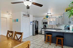 Kitchen with a kitchen breakfast bar, gray cabinetry, stainless steel appliances, decorative backsplash, and sink