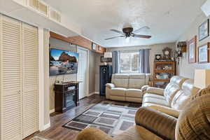 Living room featuring a textured ceiling, ceiling fan, and dark wood-type flooring