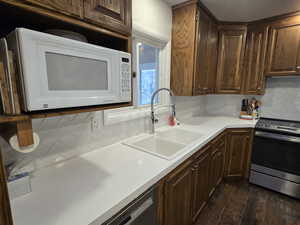 Kitchen featuring electric stove, dark hardwood / wood-style floors, tasteful backsplash, black dishwasher, and sink