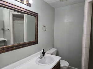 Bathroom featuring a textured ceiling, a shower with shower curtain, vanity, and toilet