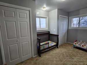 Bedroom with a crib, a textured ceiling, and light carpet