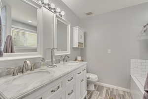 Bathroom with hardwood / wood-style flooring, tiled tub, vanity, and toilet