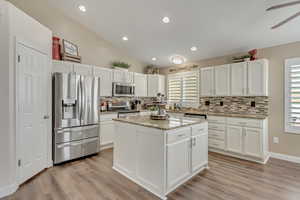 Kitchen with light stone countertops, vaulted ceiling, a center island, white cabinetry, and appliances with stainless steel finishes