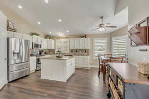 Kitchen featuring a center island, stainless steel appliances, backsplash, white cabinets, and ceiling fan