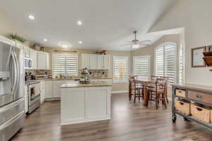 Kitchen featuring stainless steel appliances, white cabinetry, vaulted ceiling, backsplash, and a kitchen island