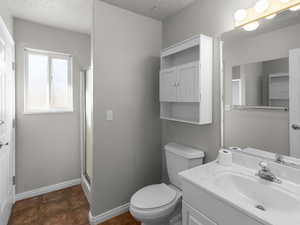 Bathroom featuring a textured ceiling, toilet, tile patterned floors, an enclosed shower, and vanity