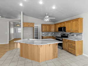 Kitchen with lofted ceiling, a kitchen island with sink, backsplash, appliances with stainless steel finishes, and sink