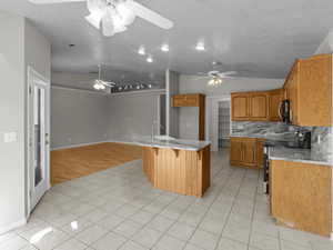 Kitchen with stainless steel electric range, lofted ceiling, decorative backsplash, and light tile patterned floors