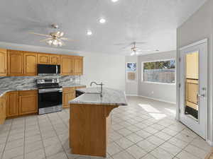 Kitchen with stainless steel appliances, sink, ceiling fan, tasteful backsplash, and a center island with sink