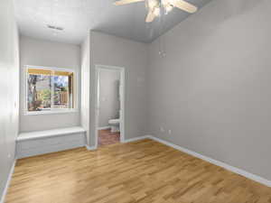 Unfurnished bedroom with connected bathroom, a textured ceiling, ceiling fan, and light wood-type flooring