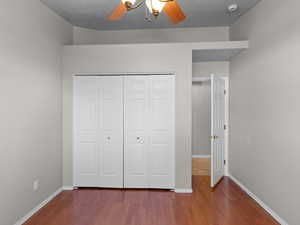 Unfurnished bedroom with hardwood / wood-style floors, a closet, ceiling fan, and a textured ceiling