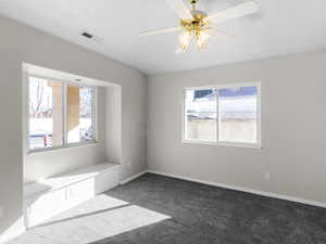 Empty room with a textured ceiling, ceiling fan, and dark colored carpet