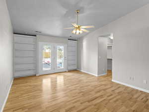 Empty room with ceiling fan, a textured ceiling, light hardwood / wood-style flooring, built in features, and lofted ceiling